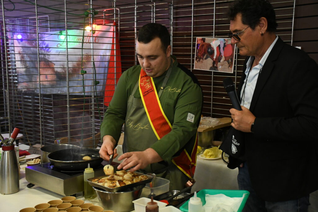 Bastien Delgado cuisinant des coquilles Saint-Jacques sous le regard de l'animateur Bruno Klimis